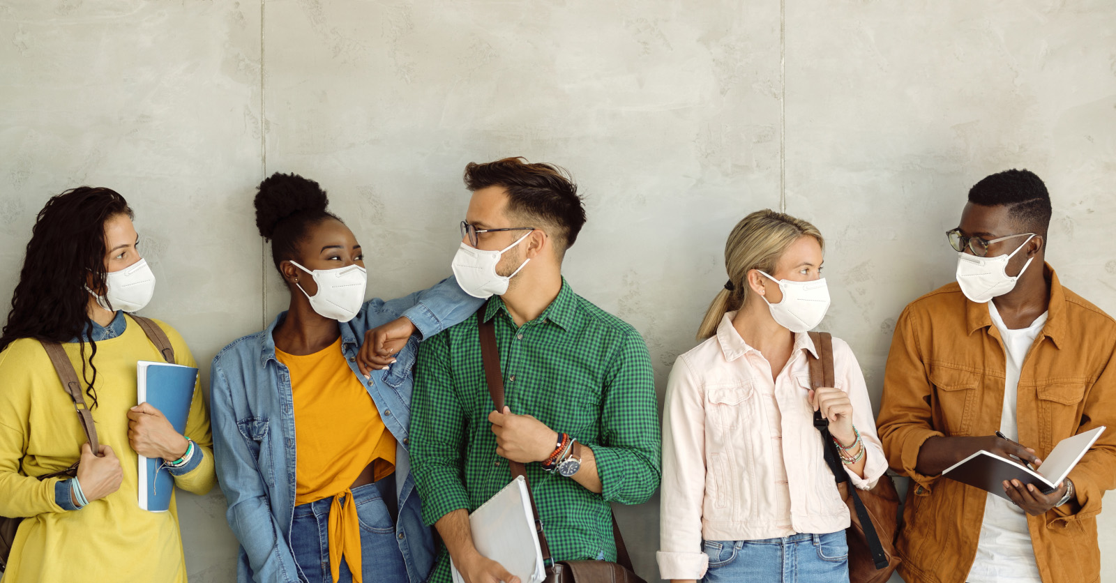 A group of college students in masks talk to each other in a hallway.